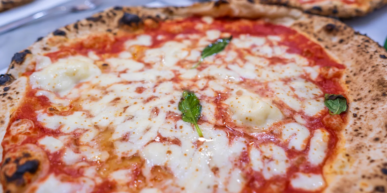 Neapolitan margherita pizza with a puffed, charred crust and fresh basil on a table in a Seville pizzeria
