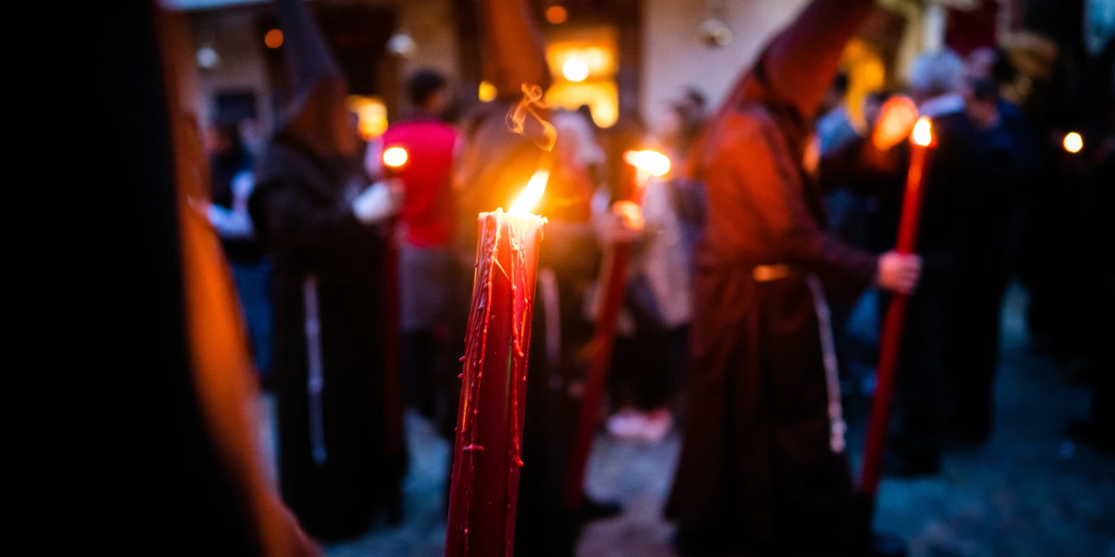 Hooded nazarenos carrying candles through a narrow street in central Seville during Holy Week