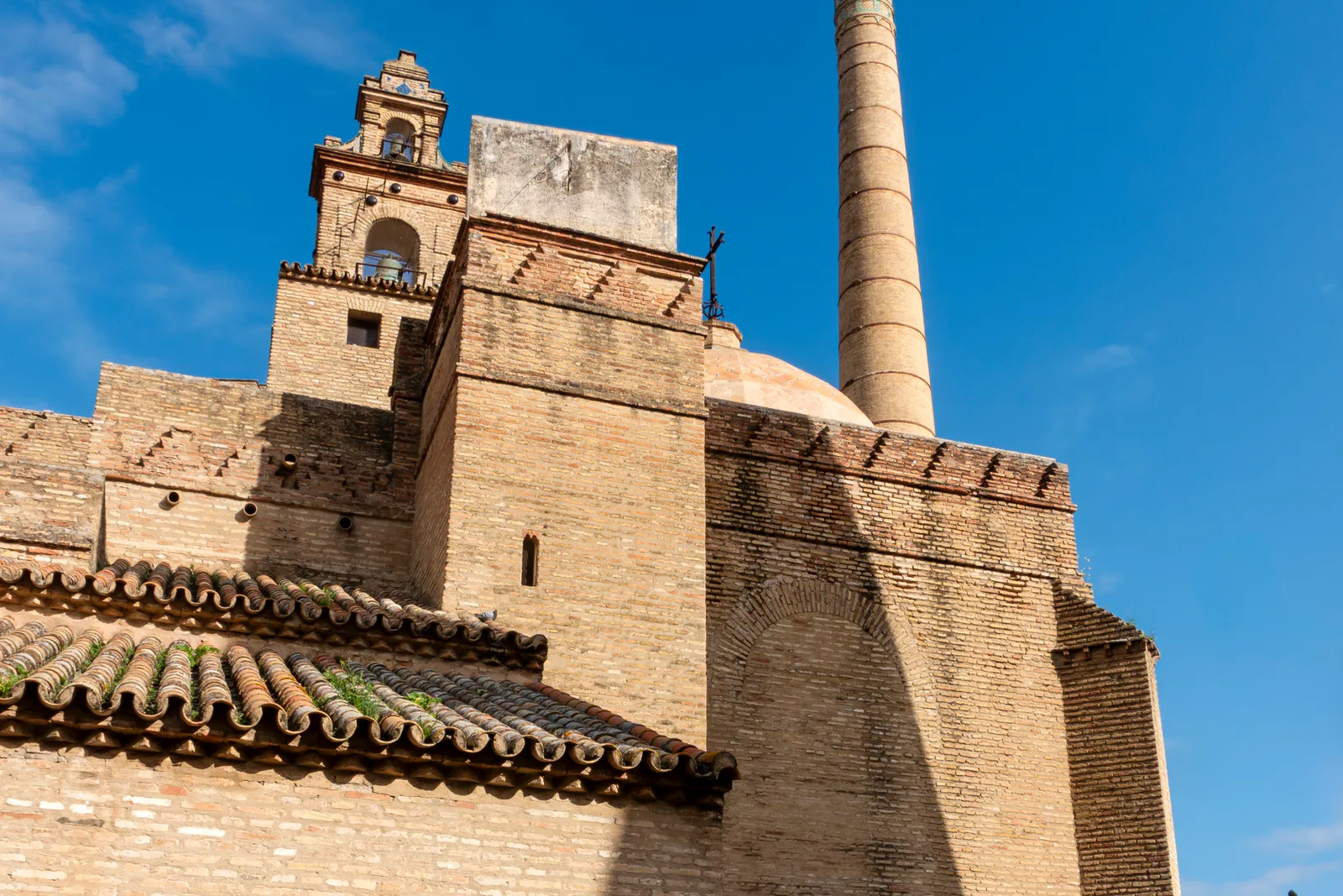 Torre de ladrillo de un antiguo monasterio junto a una chimenea industrial cónica