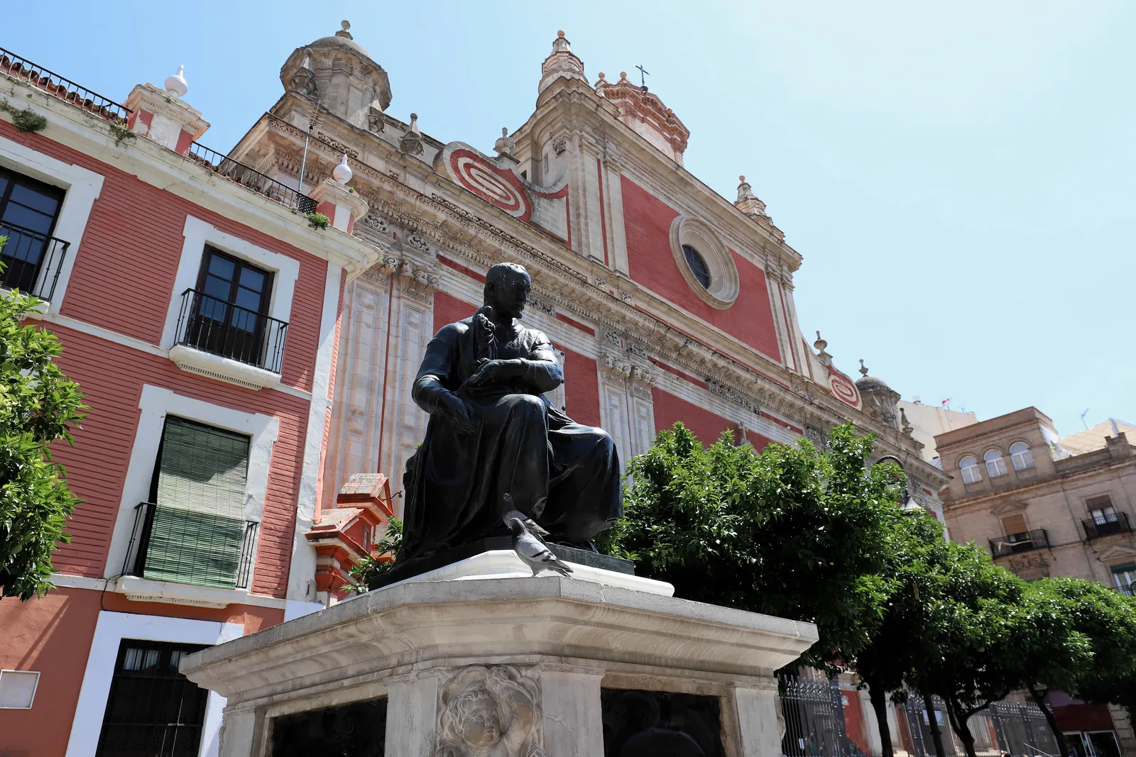 Fachada roja y blanca de una iglesia barroca con una estatua de bronce sentada delante