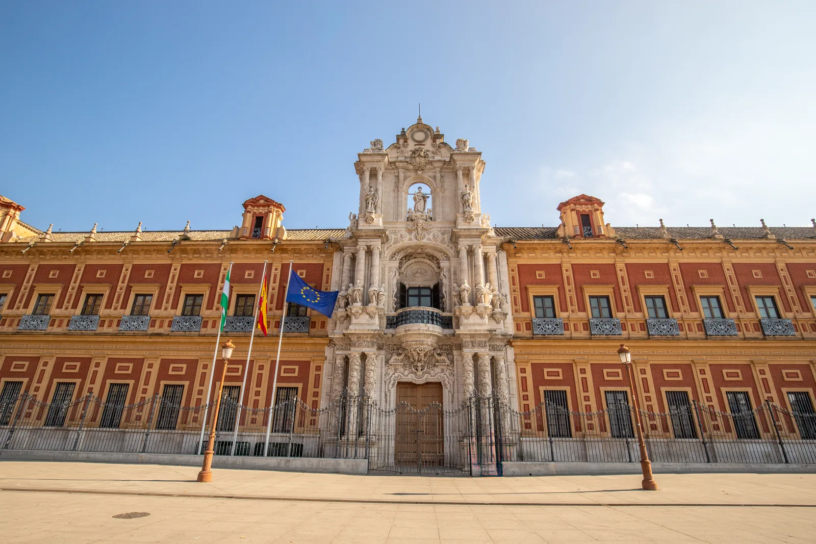 Palacio de fachada roja y amarilla con portada barroca de piedra y banderas